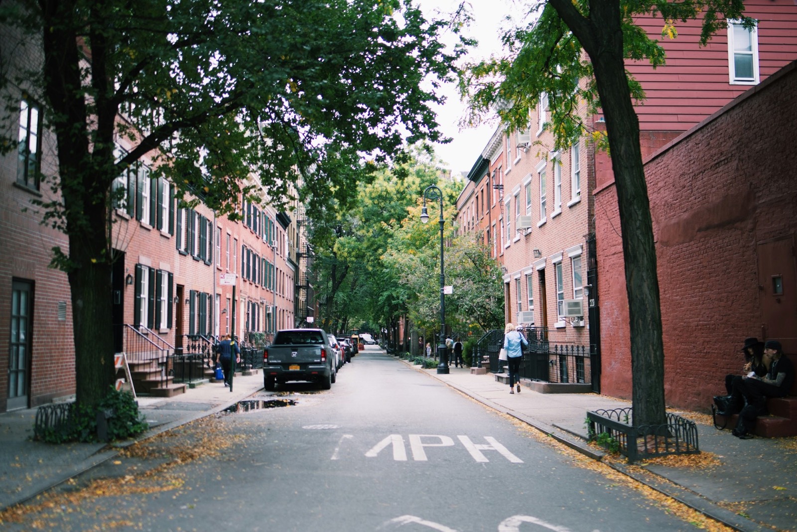 A woman walks a tree-lined West Village block of brownstones in autumn